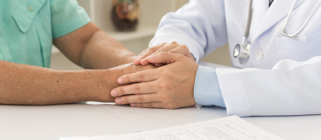 Doctor holding patient's hands as he delivers diagnosis.